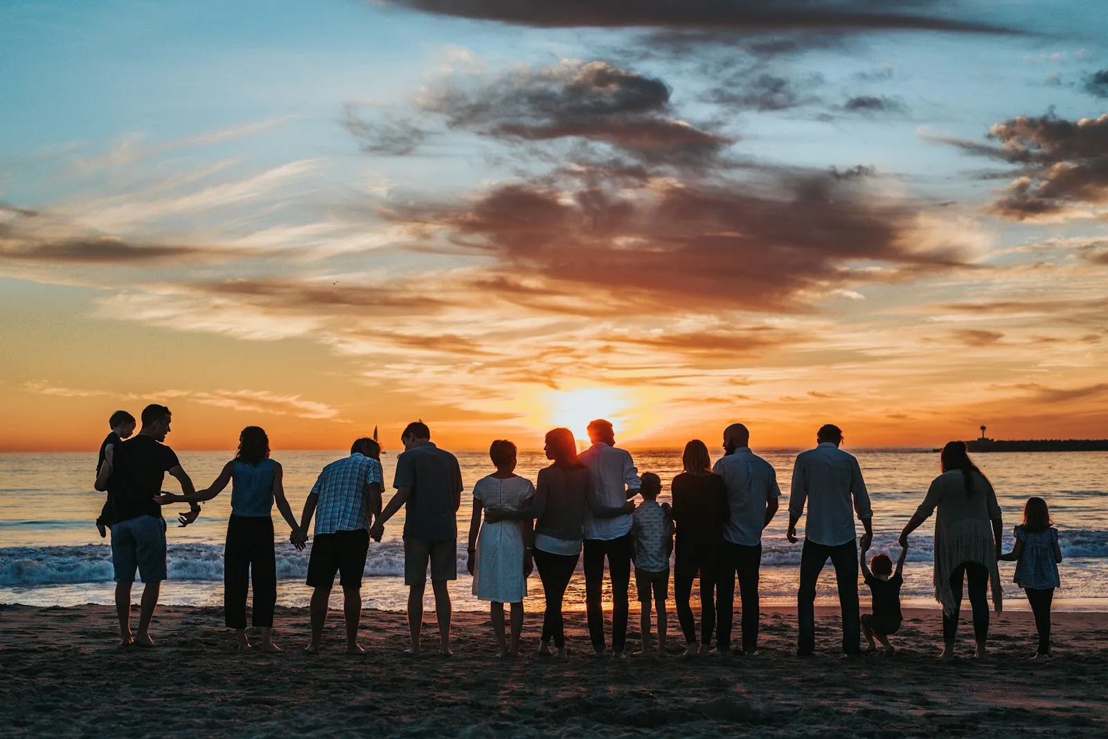 Family holding hands, silhouetted against a warm orange sunset