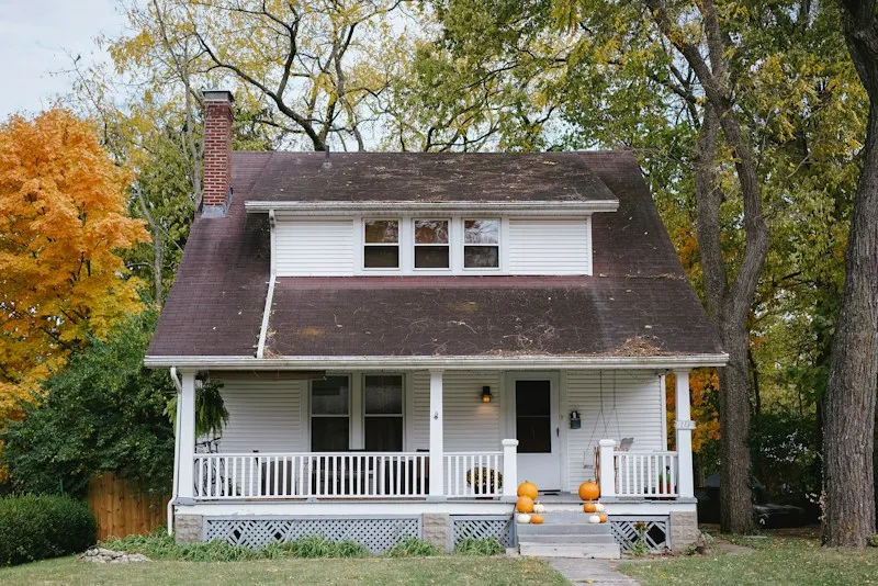 Craftsman bungalow with a covered front porch surrounded by autumn trees